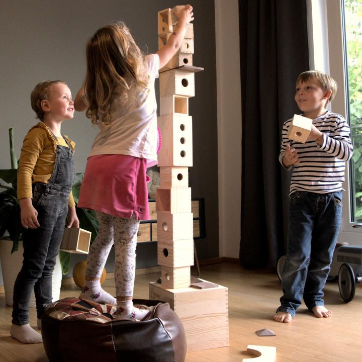 MATZBOX Kreativbaukasten: Kinder bauen einen sehr hohen Turm aus Holzbausteinen. KiTa-Spielewelt